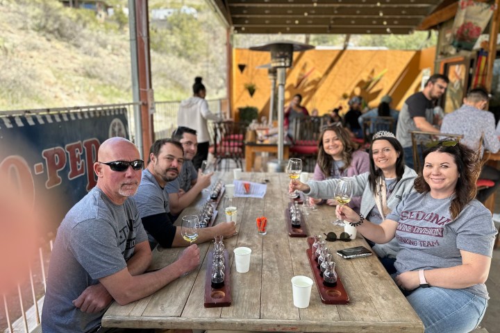Group of people sitting at an outdoor table enjoying drinks in a casual setting.