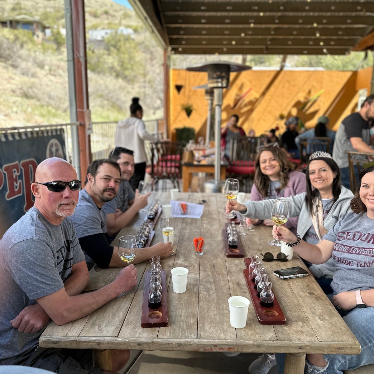 Group of people sitting at an outdoor table enjoying drinks in a casual setting.
