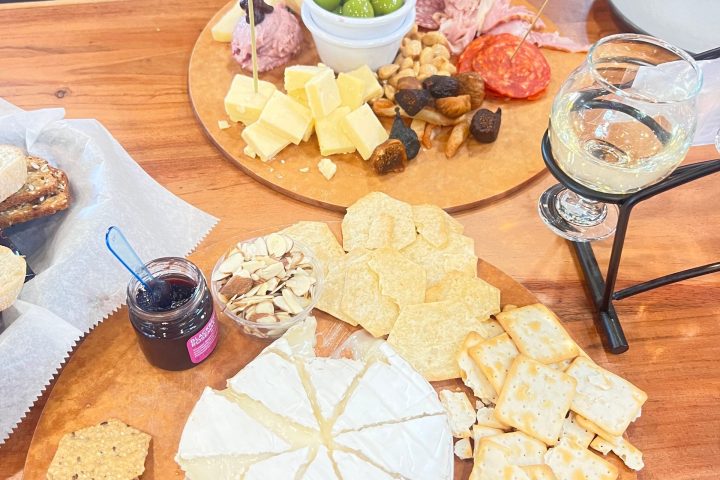 Charcuterie board with meats, cheeses, crackers, olives, nuts, and a glass of white wine on a wooden table.