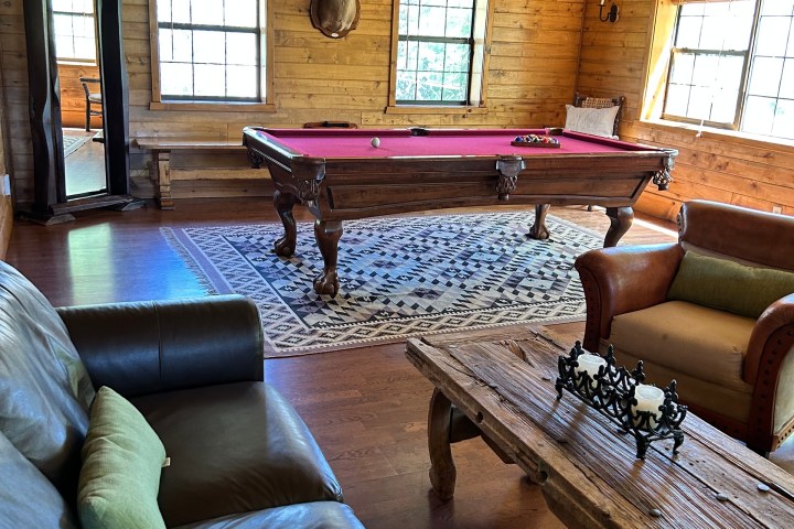 Rustic room with leather sofa, pool table, coffee table, mounted deer head, and large windows.