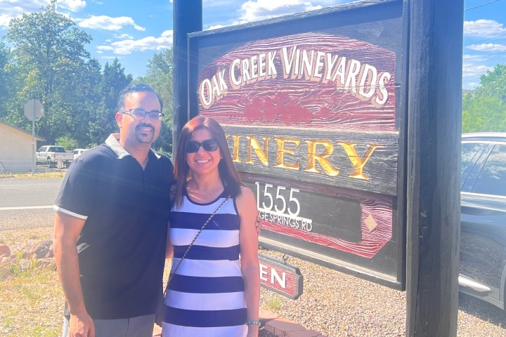 Two people smiling in front of Oak Creek Vineyards sign on a sunny day.