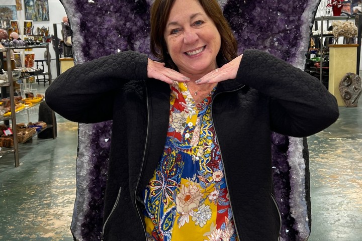 Woman posing with amethyst wings in a store, smiling with hands under chin.