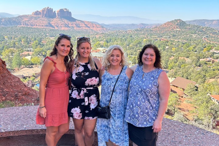 Four women posing in front of a scenic red rock landscape and blue sky.