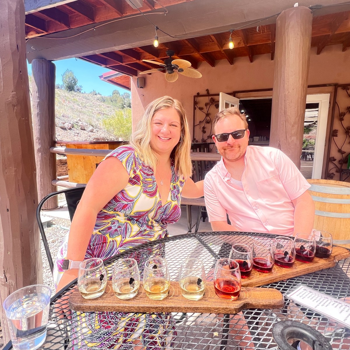 Two people sitting at a winery table outside with wine glasses on the table.