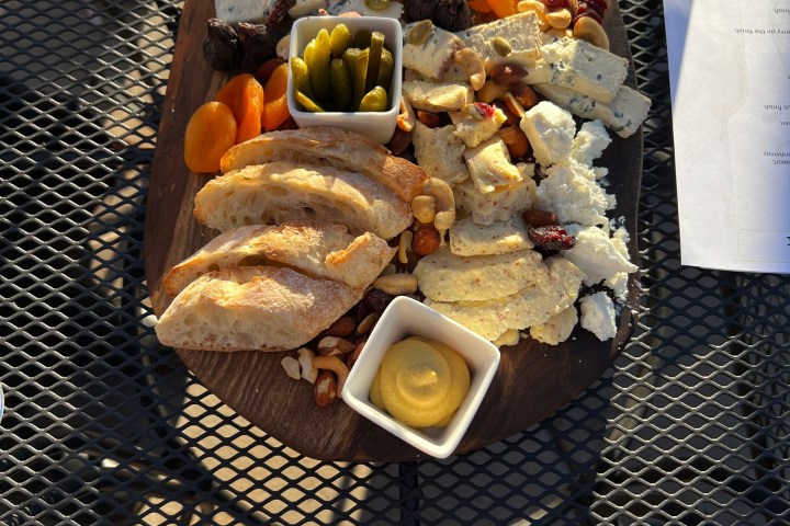 Charcuterie board with bread, cheese, nuts, pickles, and spreads on a table near a wine menu.