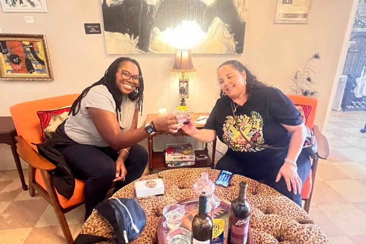 Two people clinking glasses at a table with wine in a cozy living room.