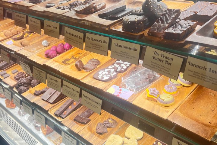 Display case with various chocolate bars and truffles on wooden trays, labeled with unique names.