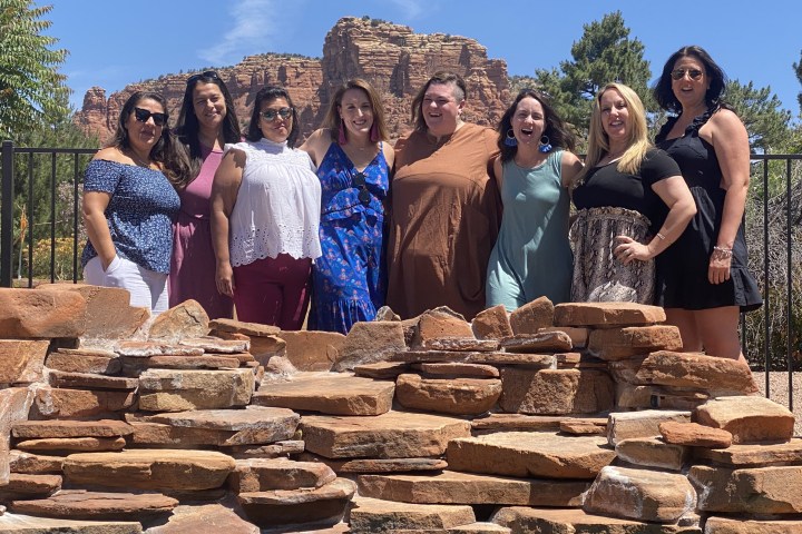 Group of women smiling by a stone wall with red rock cliffs in the background.