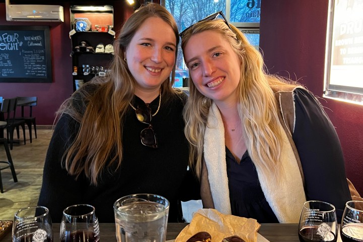 Two women smiling at a table in a restaurant with wine glasses and chocolates.