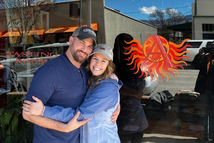 A couple hugging and smiling in front of a glass window with a sun logo and the words 'Tasting Room.'