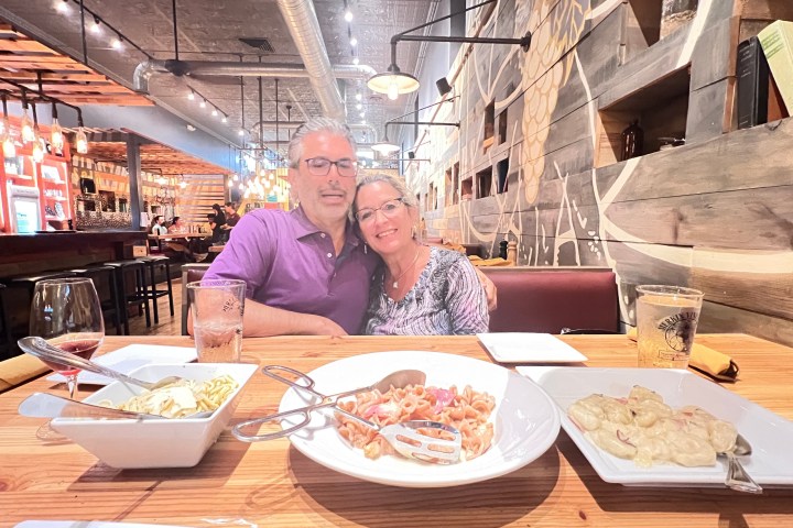 Smiling couple hugging at a restaurant table with pasta dishes and drinks.
