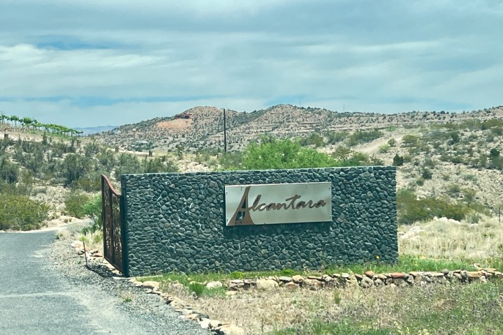Sign reading 'Alcantara' on a stone wall in a desert landscape with hills in the background.