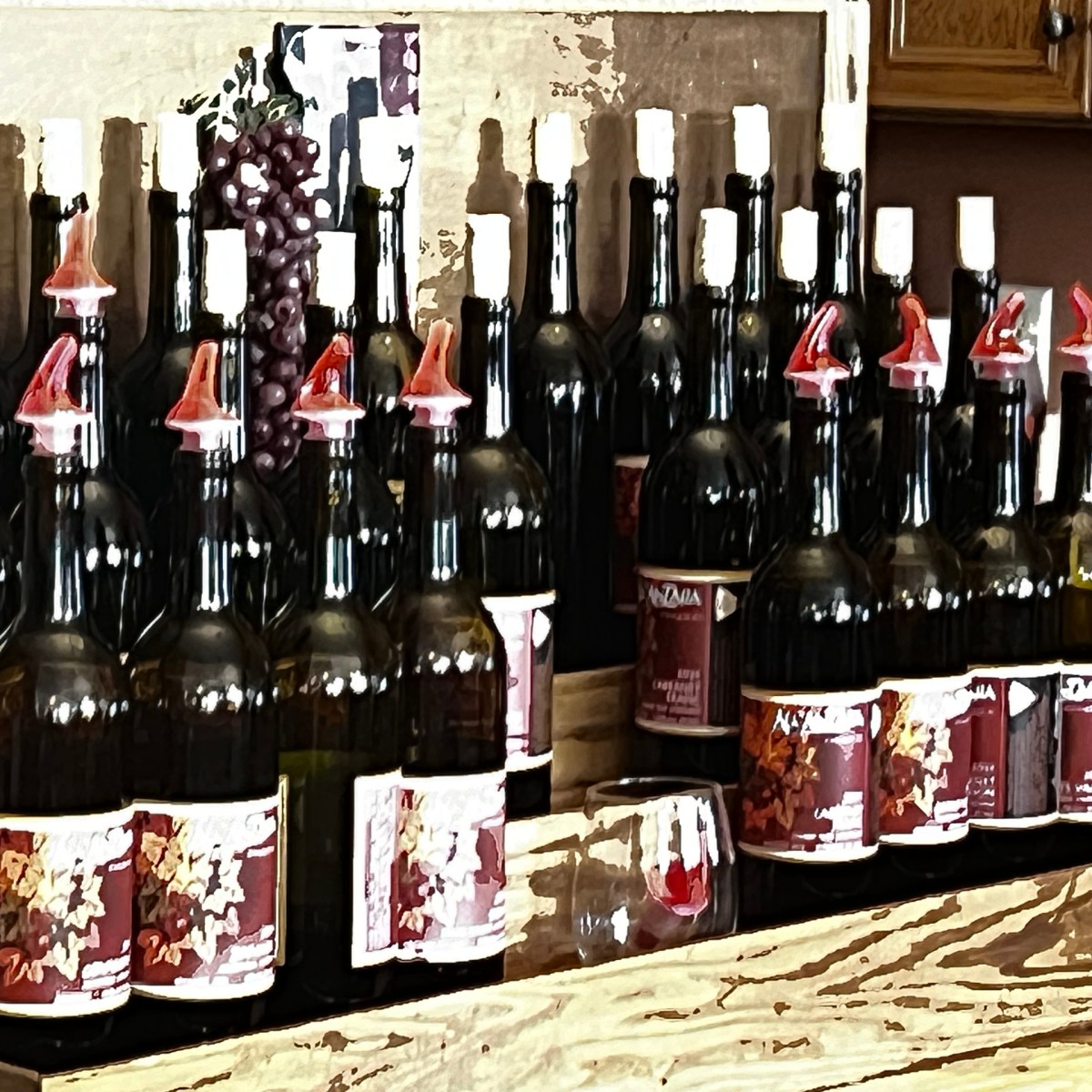 Several wine bottles on wooden shelves with red pourers and grape decor.