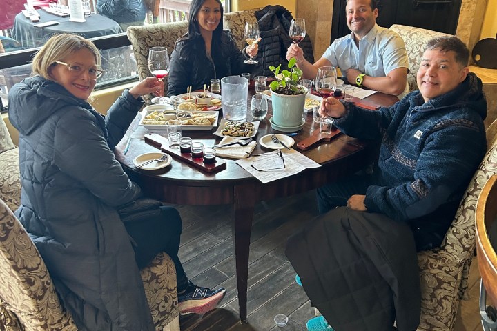 Four people dining at a round table, holding wine glasses and smiling in a cozy restaurant.