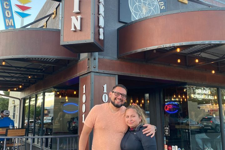 Two people smiling in front of Merkin Vineyards sign and building entrance.