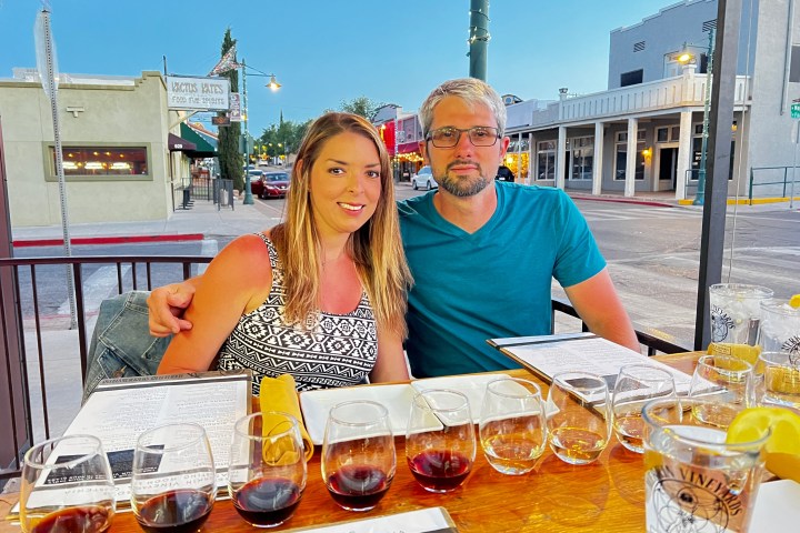 A couple at an outdoor restaurant table with wine glasses and menus.