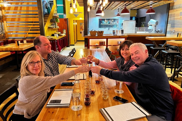 Four people toast with wine glasses at a wooden table in a cozy restaurant.