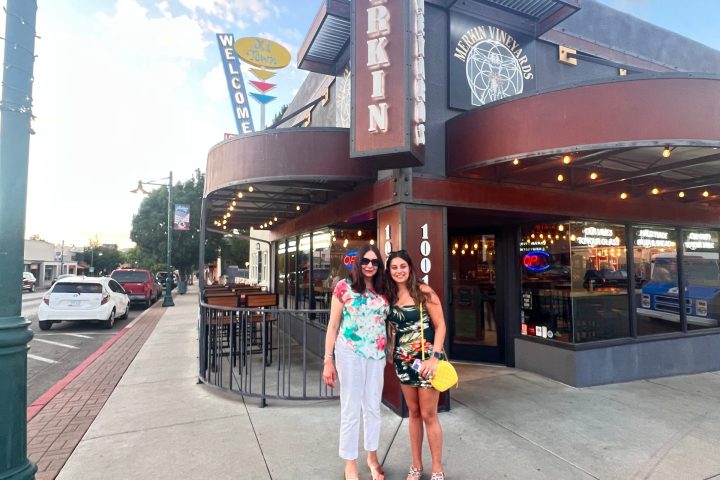Two women smiling in front of Merkin Vineyards building on a sunny day.
