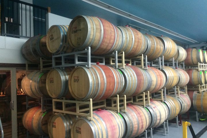 Rows of stacked wooden barrels in a storage area with blue ceiling.