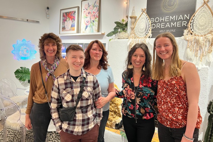 Five people smiling inside a shop with 'Bohemian Dreamer' sign and artwork on the walls.
