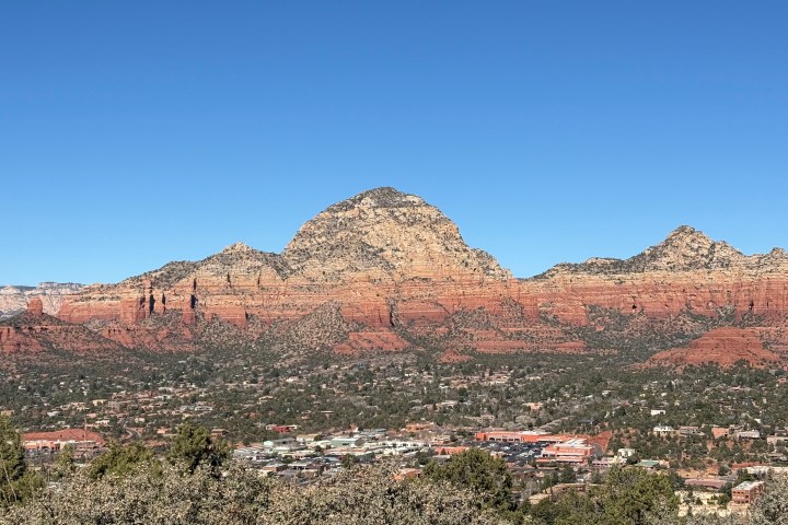 Landscape with red rock formations and a city in the foreground under a clear blue sky.