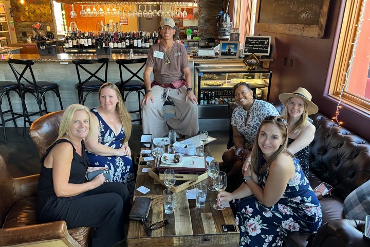 Group of people seated at a bar with wine and smiles, a server standing behind them.