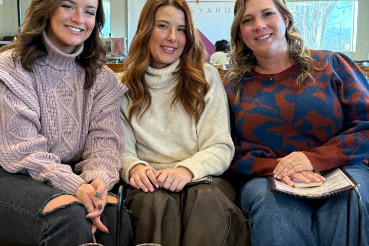 Three smiling women seated with wine flights on a table at Cove Mesa Vineyard.