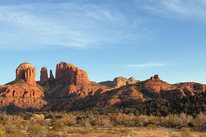 Red rock formations under a blue sky, with trees and desert landscape in the foreground.