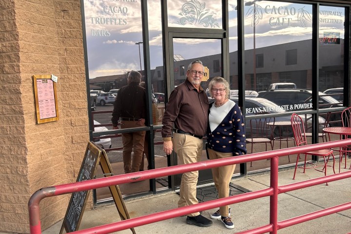 Elderly couple standing outside a storefront with a 'Cacao Café' sign.
