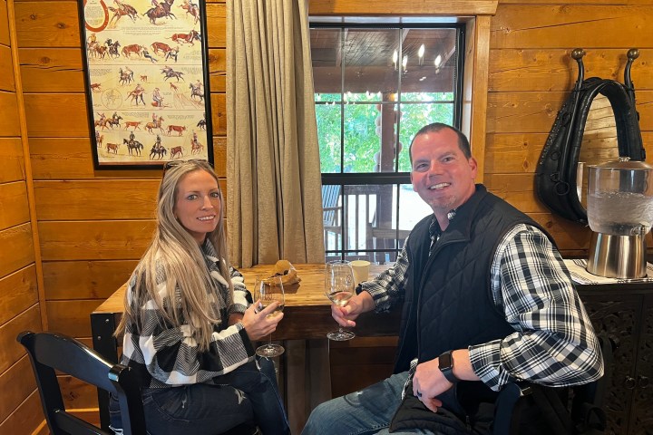 Two people sitting at a wooden table with wine glasses in a cozy rustic room.