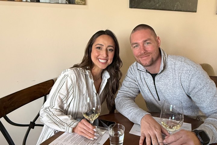 A couple at a table drinking wine, with menus and wall art in the background.