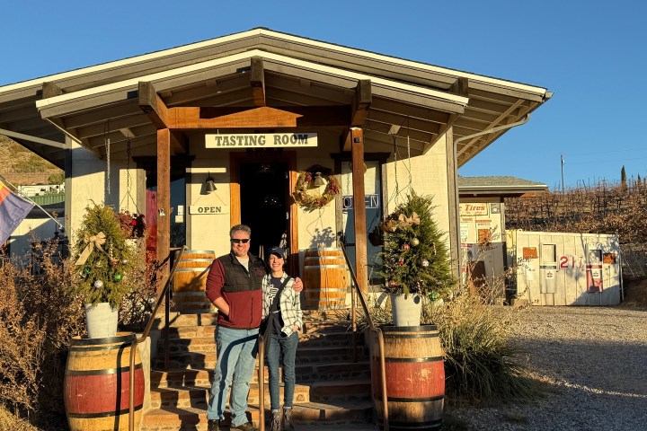 Two people stand in front of a wine tasting room entrance decorated with wreaths.