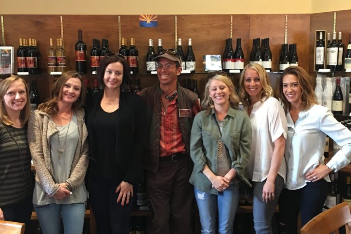 Seven people standing in front of a wine display at a wine tasting venue.