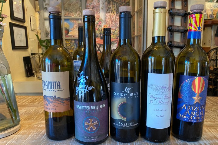 Five wine bottles with different labels on a wooden table.