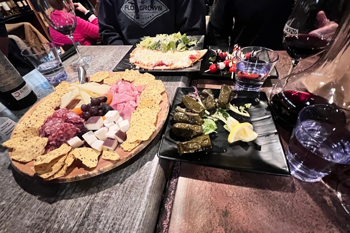 Charcuterie board and grape leaves on table with wine glasses and bottle.