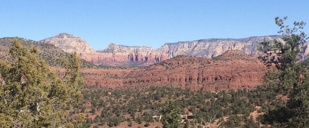 Red rock canyon landscape with scattered trees under a clear blue sky.
