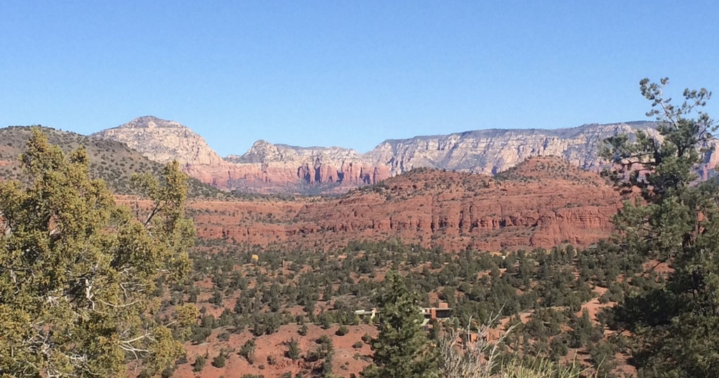Red rock canyon landscape with scattered trees under a clear blue sky.