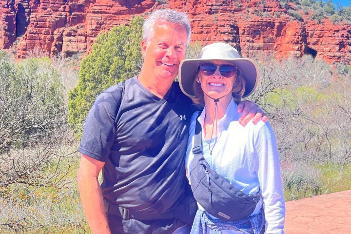 Couple posing on trail with red rock formations and clear blue sky in the background.