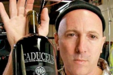 Person holding a large wine bottle labeled 'Caduceus' in a room with studio equipment.