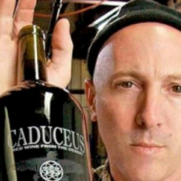 Person holding a large wine bottle labeled 'Caduceus' in a room with studio equipment.