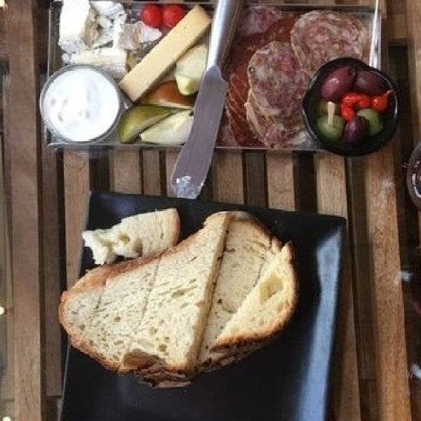 Table with wine glasses, sliced bread, cheeses, salami, olives, and dips on plates.