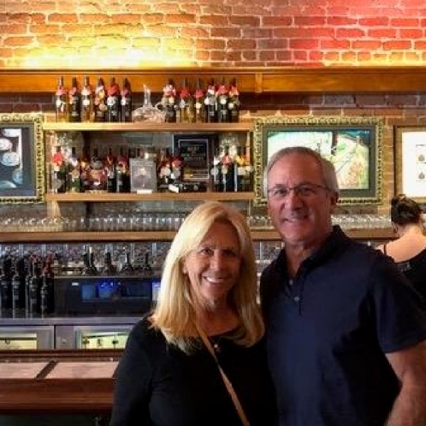 A smiling couple standing in front of a bar with bottles and glasses.