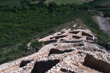 Ruins of ancient stone structures on a hillside with green vegetation in the background.