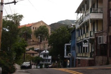 Hilly street with houses, trees, and power lines under an overcast sky.