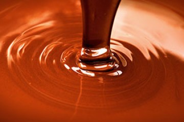 Molten chocolate being poured, creating ripples in a smooth, glossy surface.