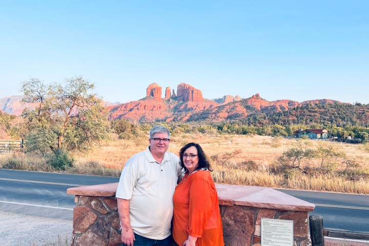 Couple posing in front of red rock formations under clear blue sky.