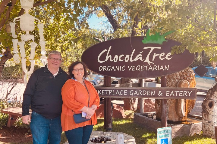 Two people standing beside ChocoláTree Organic Vegetarian sign with a skeleton decoration hanging nearby.
