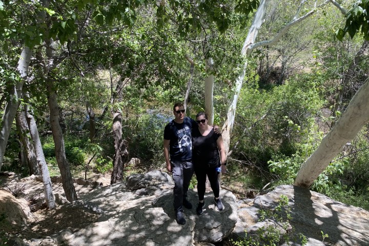 Two people standing on a rocky path in a leafy forest.