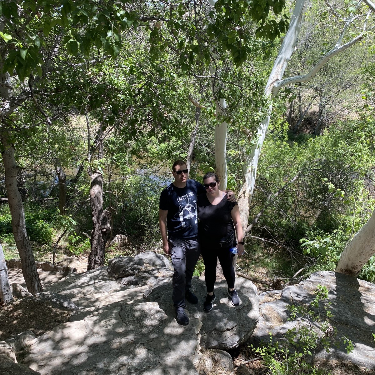 Two people standing on a rocky path in a leafy forest.