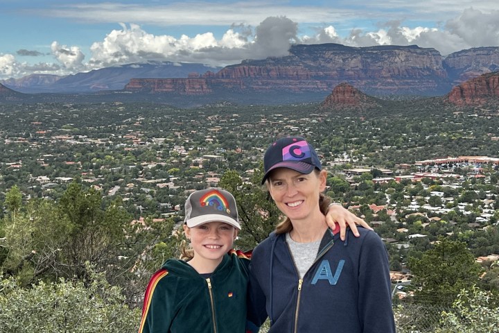 Two people pose with arms around each other, against a backdrop of mountainous landscape and cloudy sky.